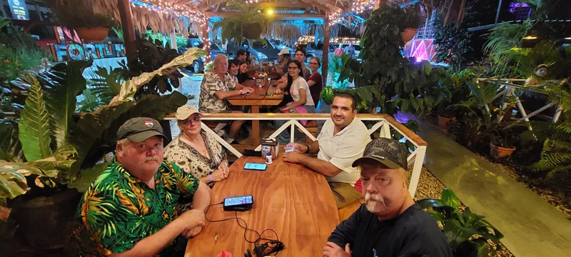 A group sits around a long wooden table at night, under strings of lights.