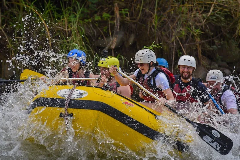 A group in helmets and life jackets paddles a yellow raft through whitewater.