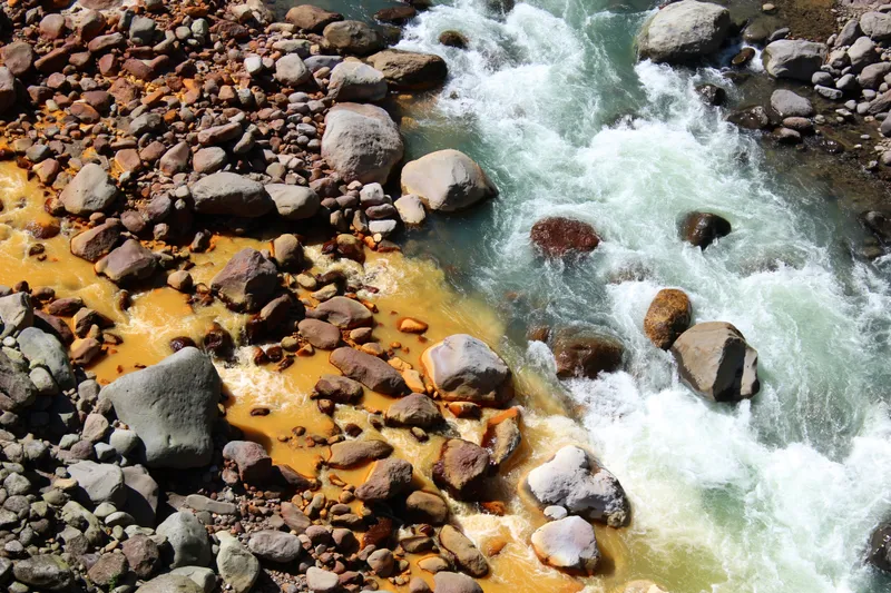The yellow water of the Sucio river meets a clear one over pale stones.