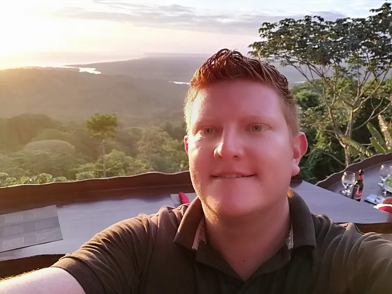 A man at a lookout table, forest and sea behind him.