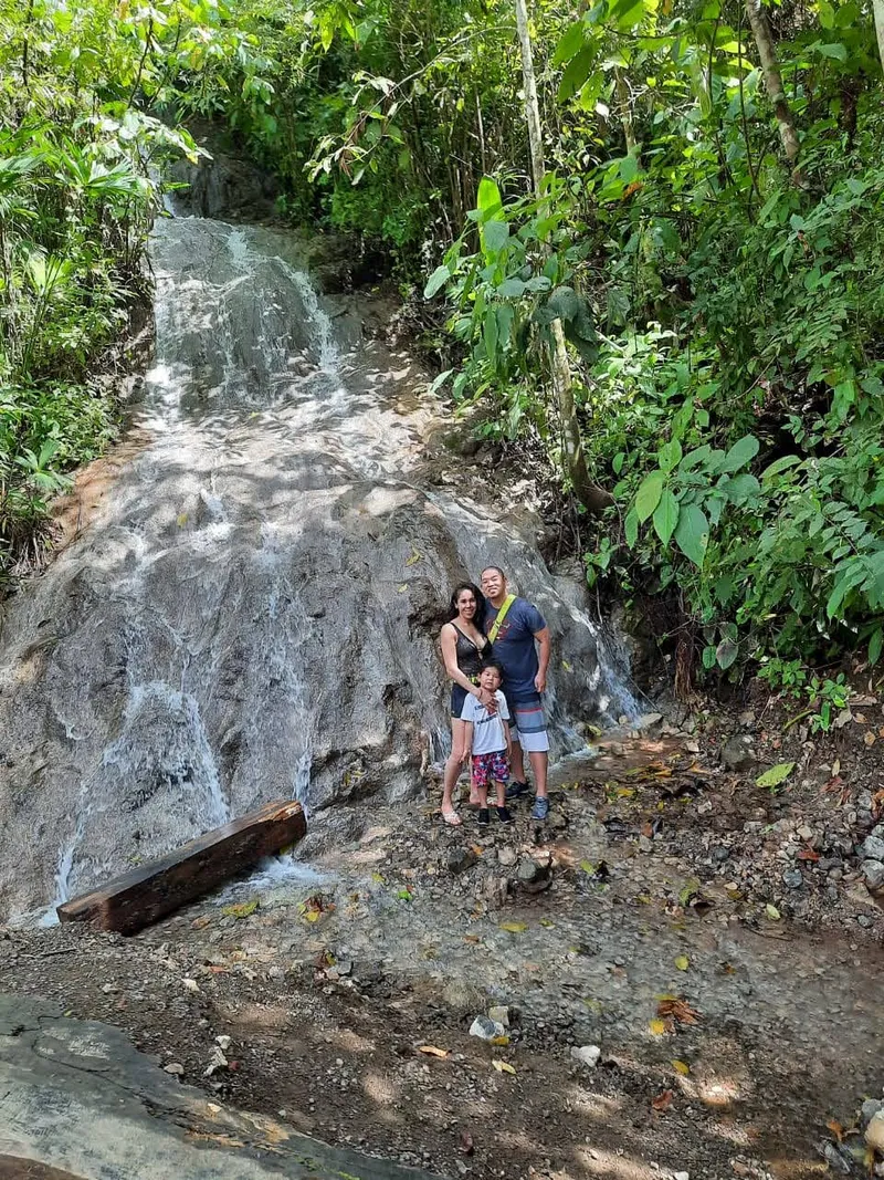 A family stands at the foot of a waterfall running over pale rock.