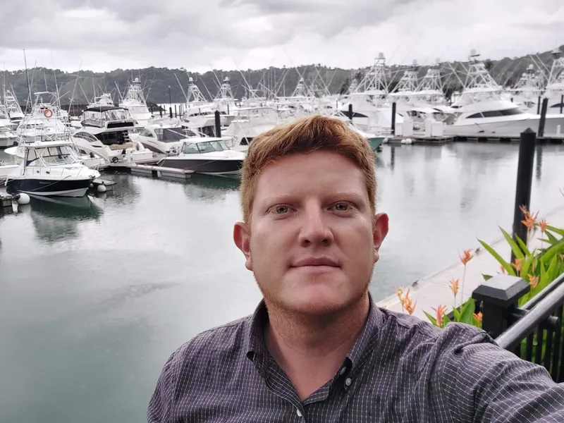 A man photographed close up at a marina, sport fishing boats moored behind him.