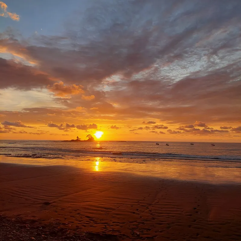 Sunset over a wide flat beach, the sun mirrored on the wet sand.
