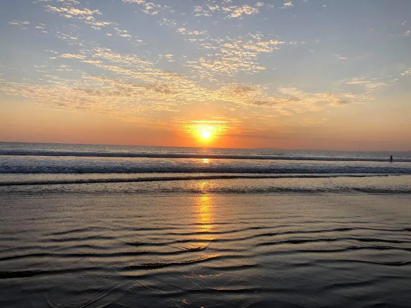 Low waves reach a dark beach while the sun touches the horizon.