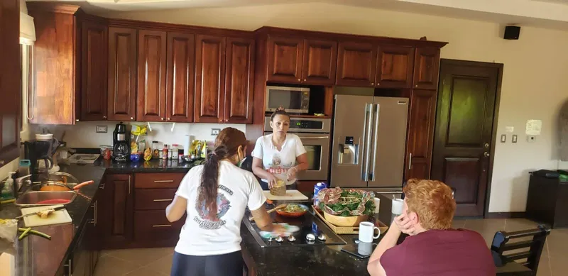 Two women cook together at the island of a kitchen with dark wood cabinets.