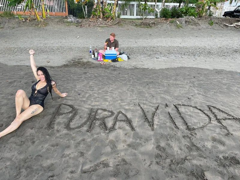 The words Pura Vida written large in the sand, a woman sitting beside them.