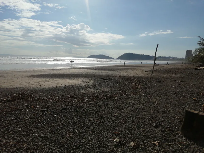 Low tide on a dark sand beach, with two rounded islands on the horizon.