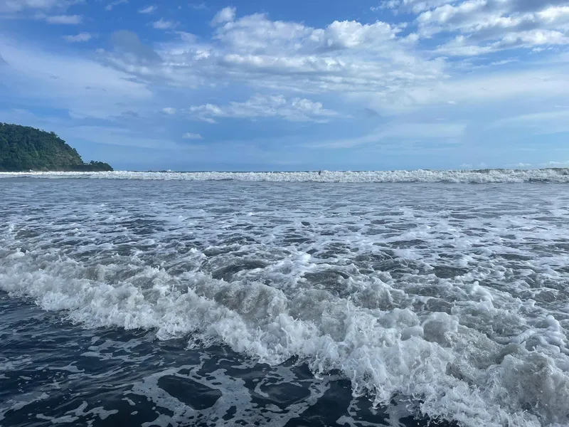Surf breaking in long white lines under a sky of scattered clouds.
