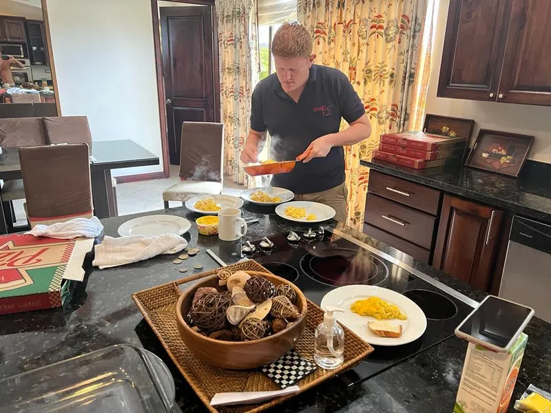 A man serves food from a pan onto plates at a kitchen counter.