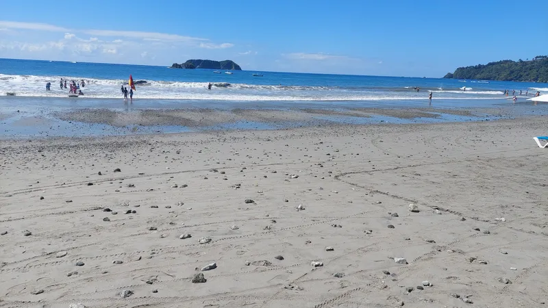 Wet sand at low tide with a rocky island offshore and a few people at the water.