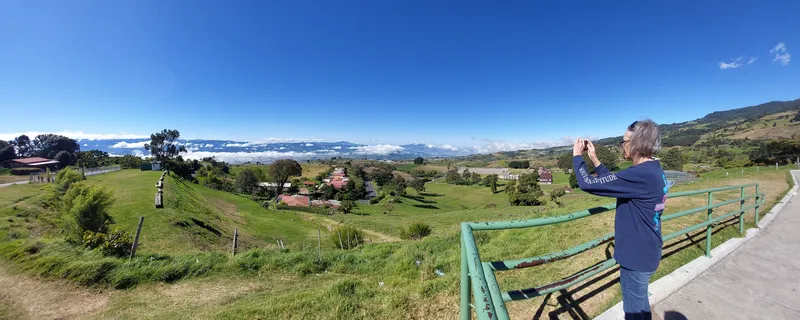 A small town of red roofs and green fields seen from a hillside, with a metal gate at the edge of the frame.