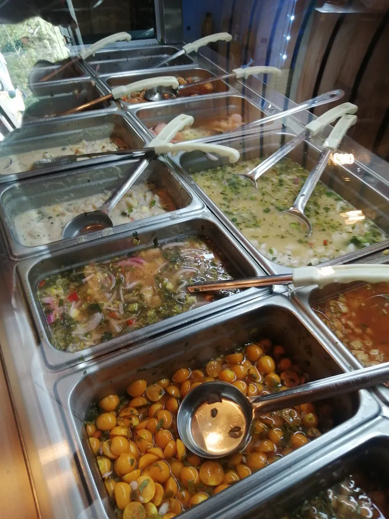 Metal buffet trays with ladles and tongs, holding chopped salads, stews and small orange fruit.