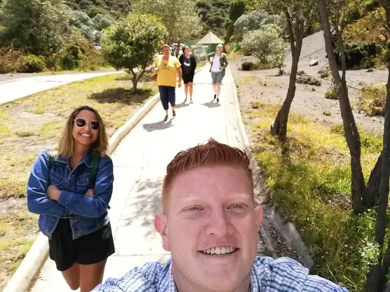A selfie on a paved path, a woman in a denim jacket to one side and three people walking down toward the camera.