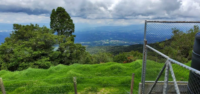 Green pasture and a wire fence in front, with a wide valley of scattered towns under low cloud.