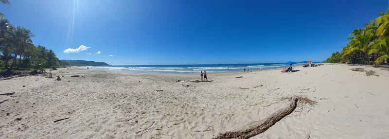 A wide sandy beach under a clear blue sky, with a few distant figures at the waterline.