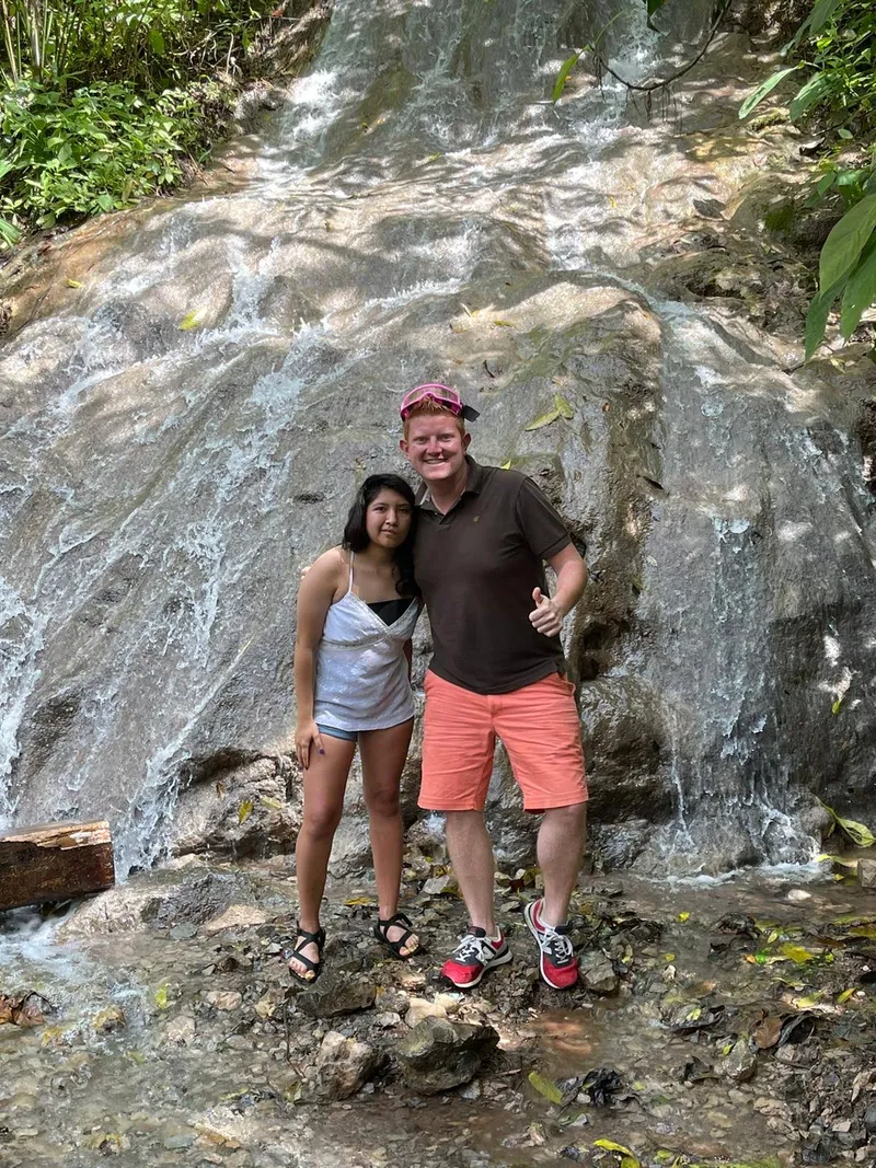 A couple poses against a pale rock wall with water running down it.