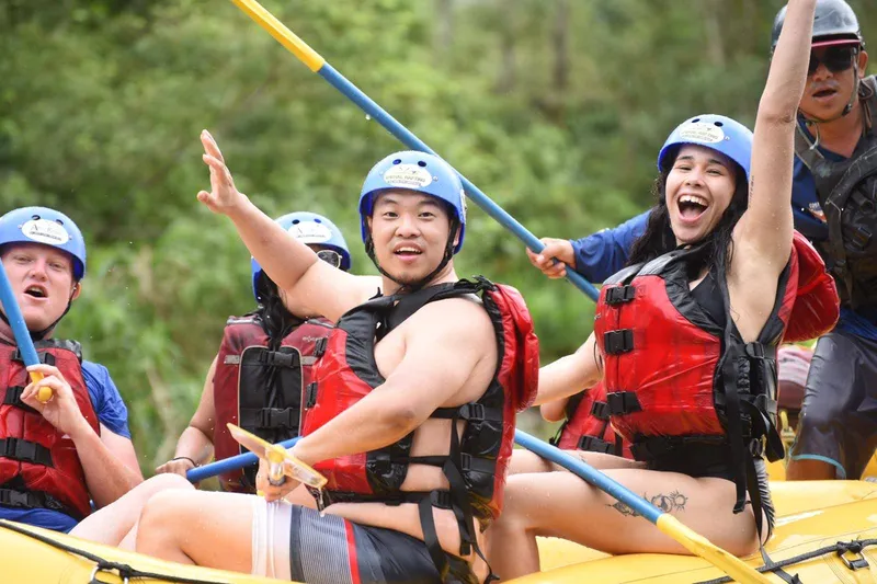 Rafters in blue helmets and red life jackets sit on a yellow raft, one of them raising an arm.
