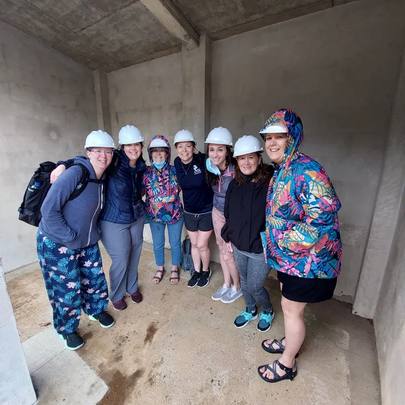 Seven visitors in white hard hats stand together inside a bare concrete shelter.