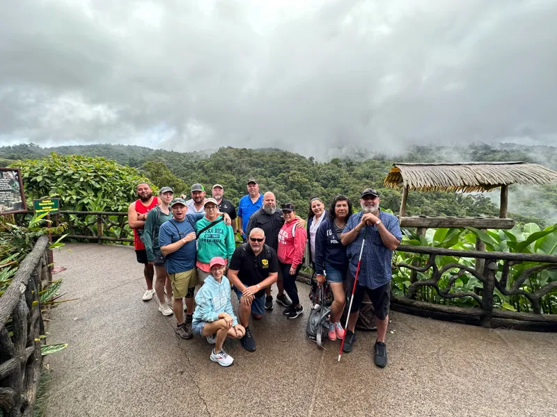 A large group poses on a paved lookout with forest and low cloud behind them.