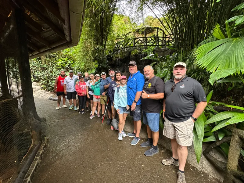 A group lines up along a garden path with a stone footbridge and bamboo behind.
