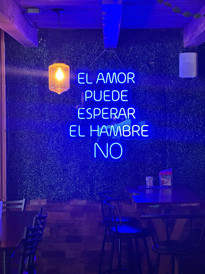 A blue neon sign in a dark room reads that love can wait but hunger cannot.