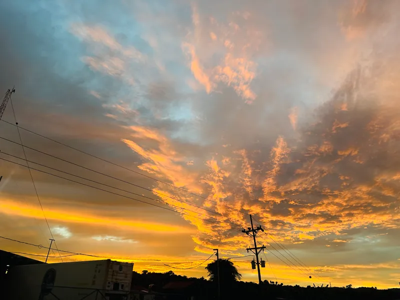 Orange clouds spread across the sky at sunset, above power lines and low rooftops.